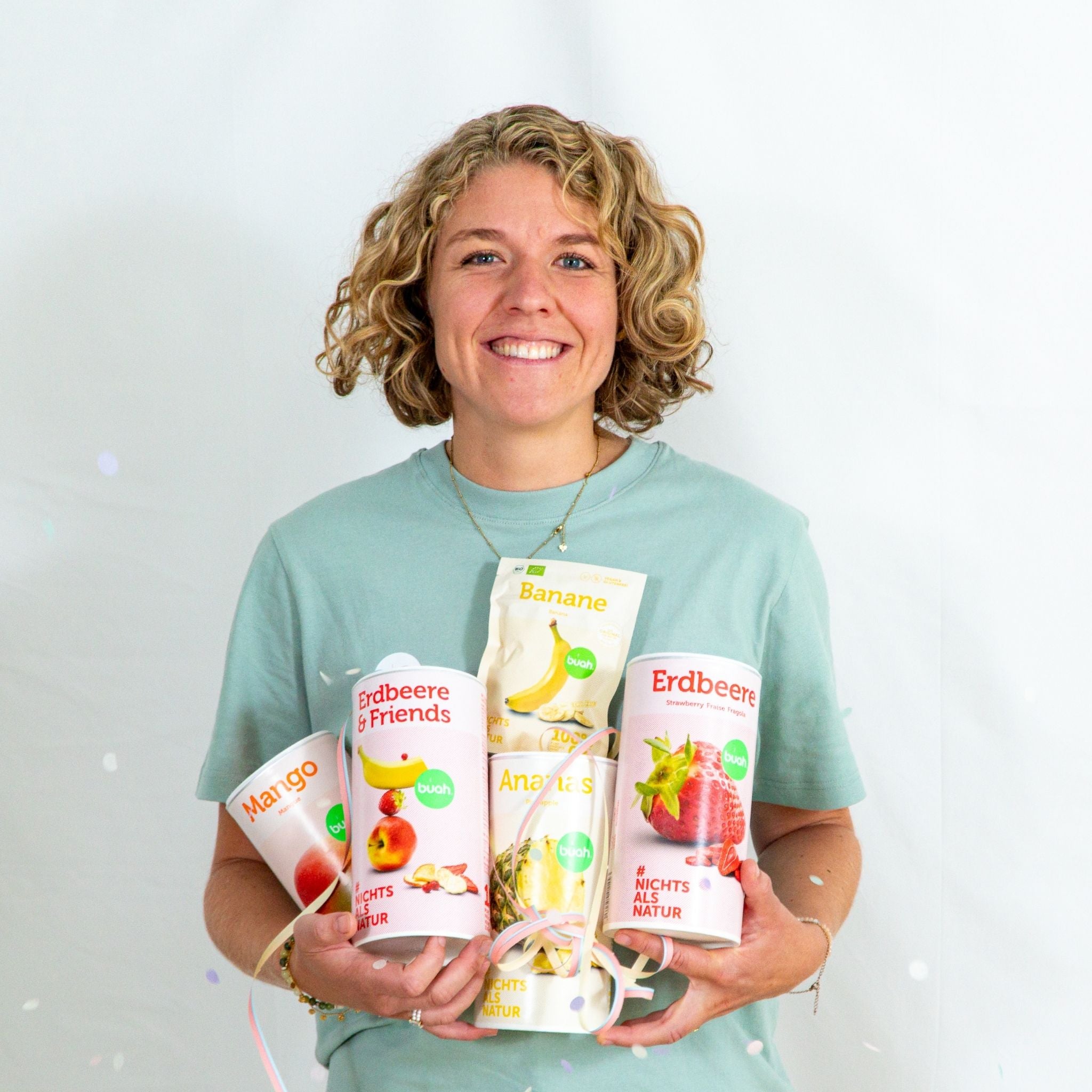 Jessica Gruenderin von buah in gruenem buah Shirt mit buah gefriergetrockneten Fruechten in der Dose im Arm - Konfetti und Luftschlangen im Hintergrund fuer den buah Birthday