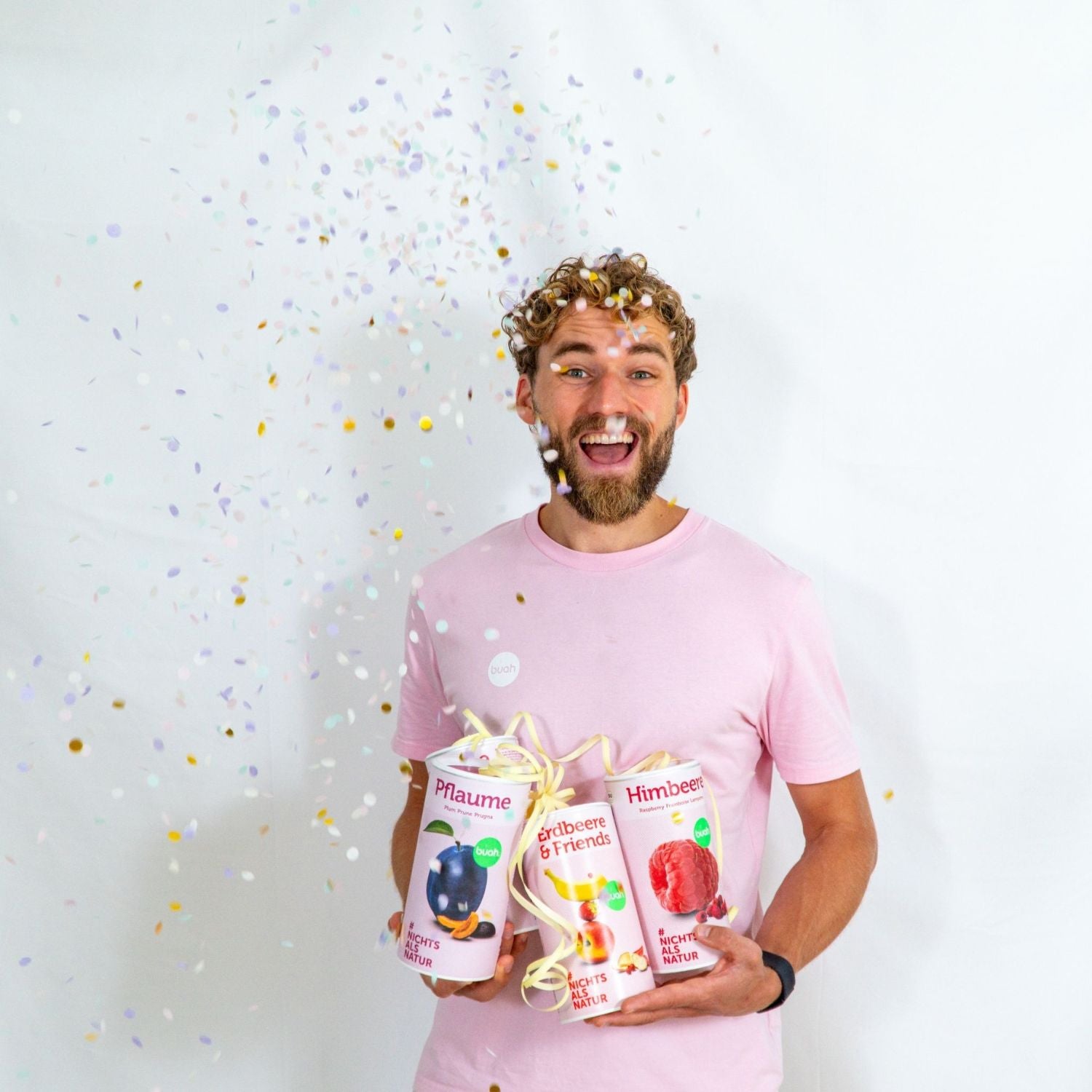 Daniel Gruender von buah in rosa buah Shirt mit buah gefriergetrockneten Fruechten in der Dose im Arm - Konfetti und Luftschlangen im Hintergrund fuer den buah Birthday