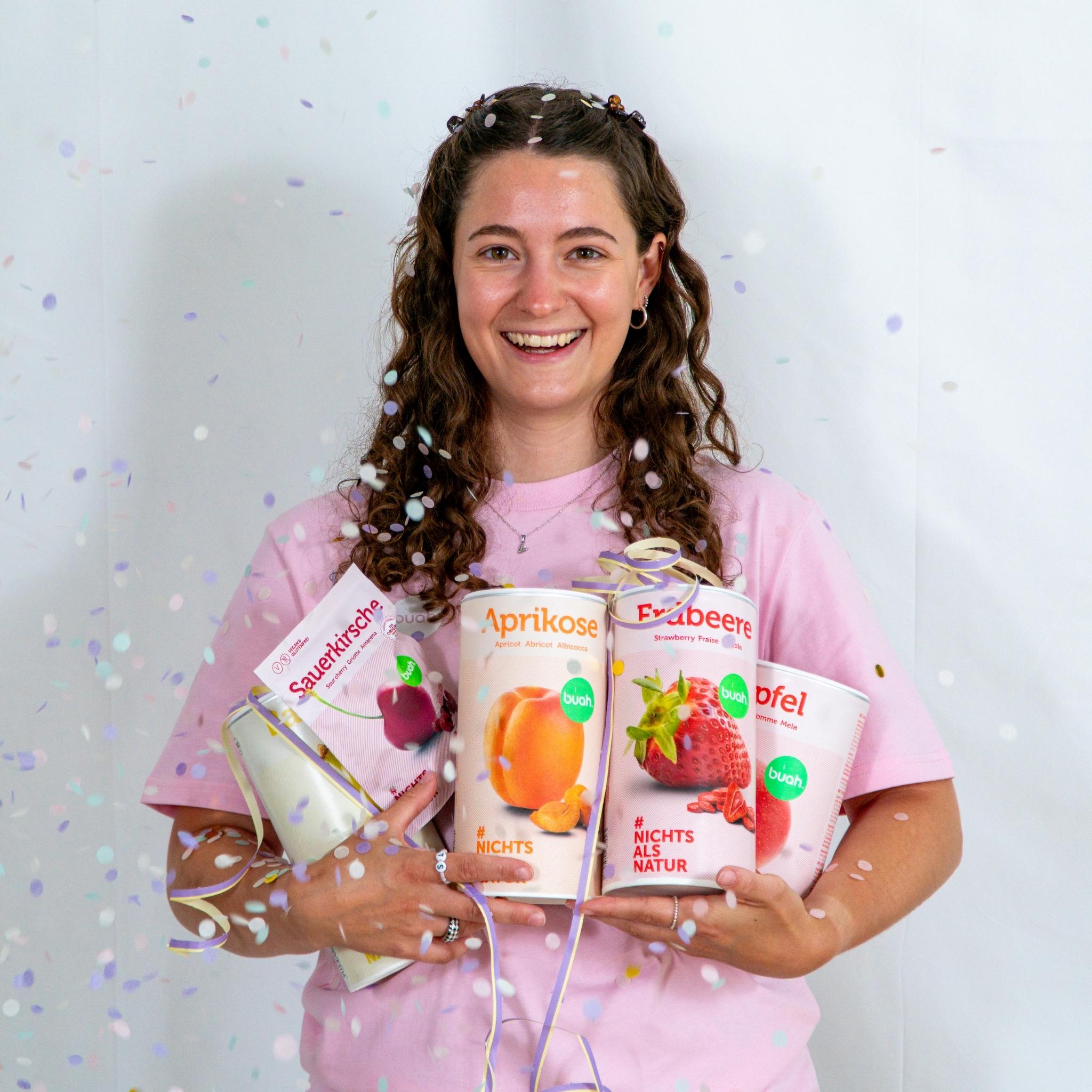 Vanessa von buah im rosa buah Shirt mit buah gefriergetrockneten Fruechten in der Dose im Arm - Konfetti und Luftschlangen im Hintergrund fuer den buah Birthday