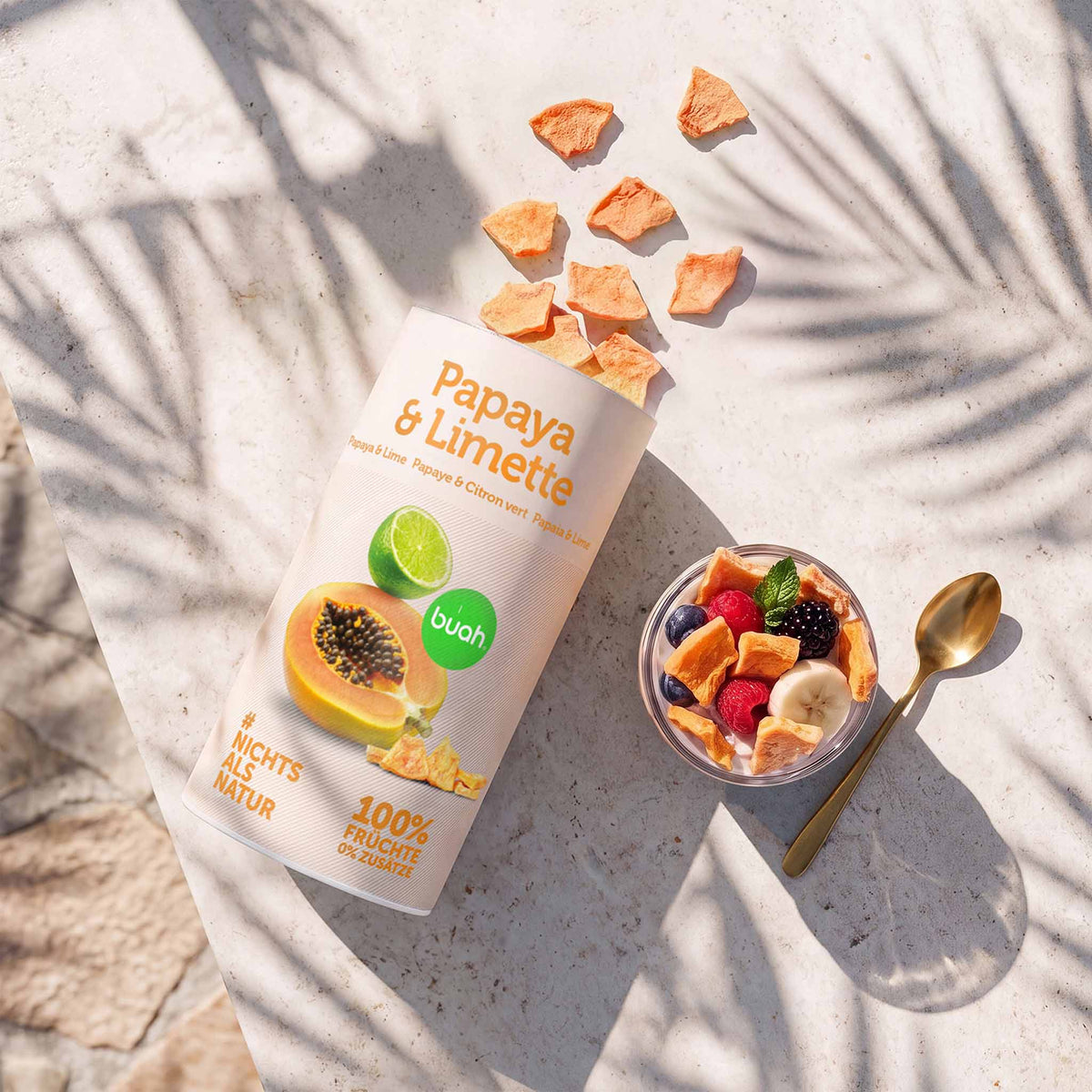 buah-Dose „Papaya & Limette“ mit gefriergetrockneter Papaya und Limette neben einer Schale mit Joghurt, Beeren, Banane und knusprigen Papayastückchen.