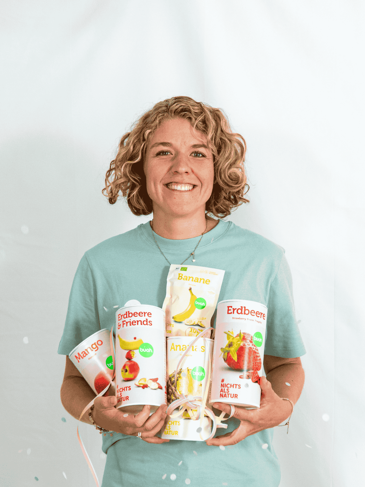 Jessica Gruenderin von buah in gruenem buah Shirt mit buah gefriergetrockneten Fruechten in der Dose im Arm - Konfetti und Luftschlangen im Hintergrund  fuer den buah Birthday