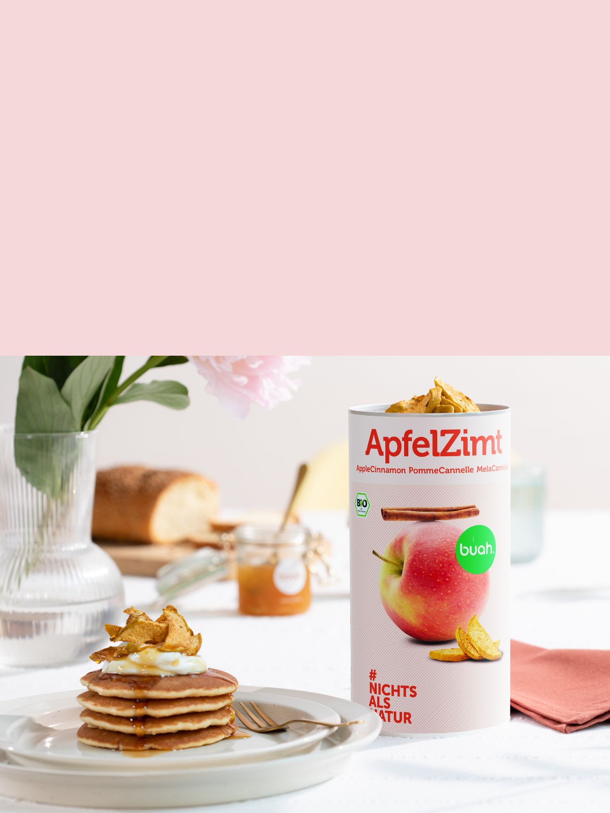 Splitscreen mit rosa Hintergrund oben und Bild von Pancakes auf einem Teller getoppt mit buah AfelZimt und einer Dose ApfelZimt daneben 
