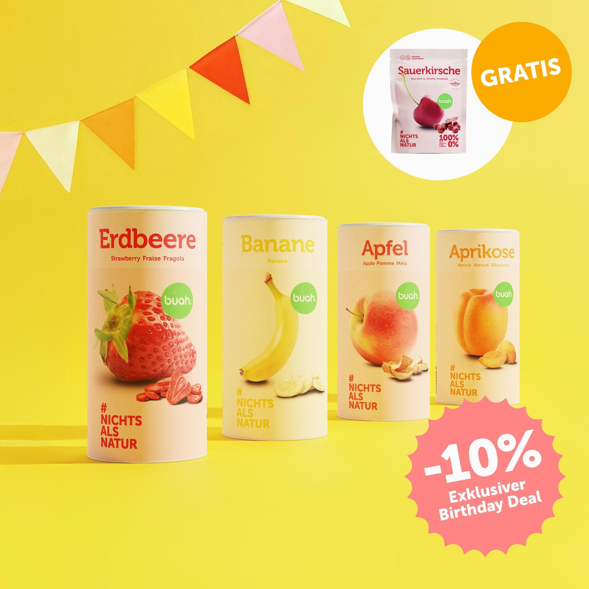 buah Birthday Set mit buah gefriergetrockneter Erdbeere in der Dose, Banane, Apfel und Aprikose vor gelbem Hintergrund mit bunten Girlanden im Hintergrund, 10% Badge im Bild