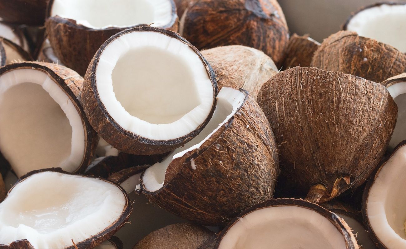 Nahaufnahme vieler aufgeschnittener brauner Kokosnuesse mit weißem Fruchtfleisch, die auf und nebeneinander liegen 