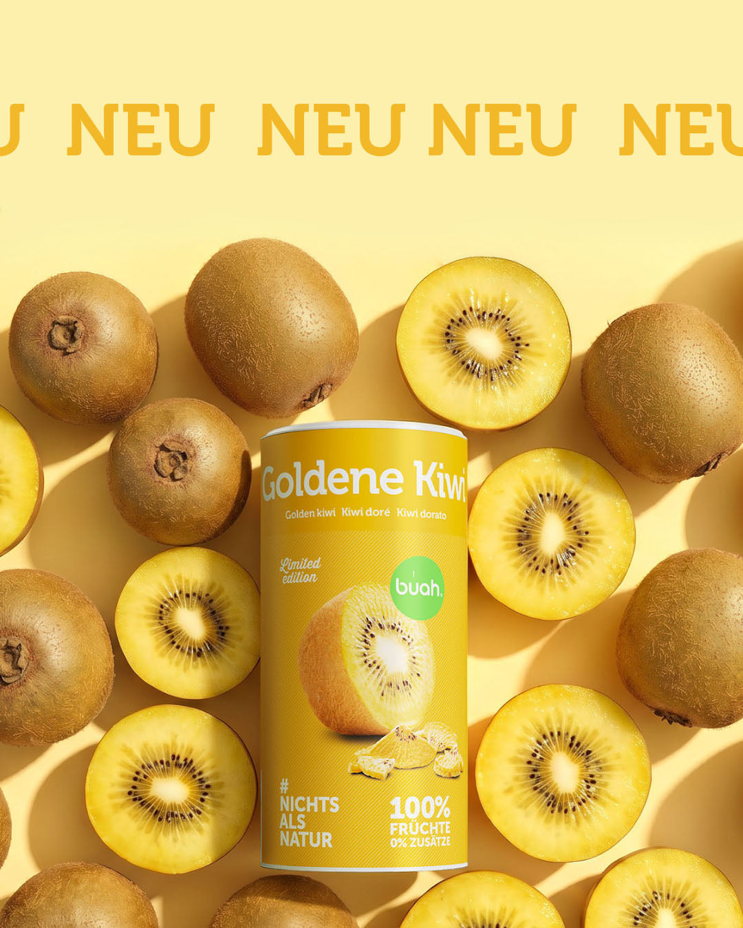 Eine gelbe Dose buah gefriergetrocknete Goldene Kiwi liegt umgeben von frischen, aufgeschnittenen Kiwis auf einem gelben Hintergrund. Am oberen Bildrand steht groß das Wort „NEU“.