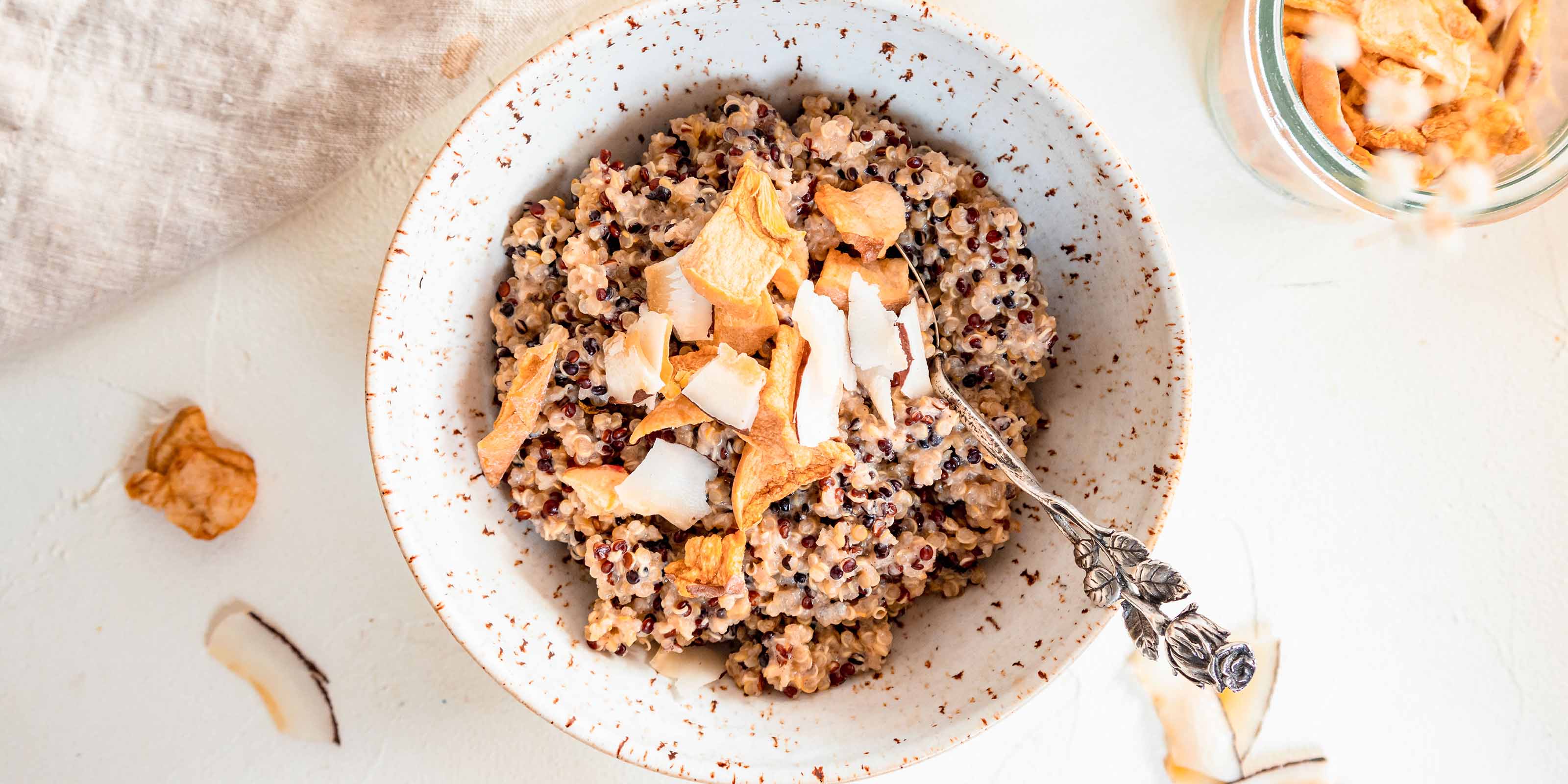 Quinoa Porrdige mit buah Kokoschips und buah Ananas in einer weißen Schale angerichtet 