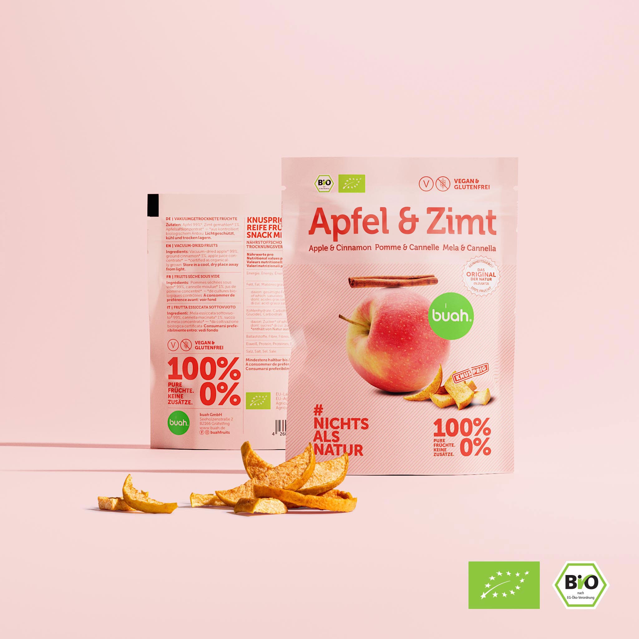 Ein kleiner Beutel buah gefriergetrocknete Früchte der Sorte Apfel & Zimt steht vor einem rosa Hintergrund. Daneben steht links ein zweiter Beutel, der die Rückseite mit den Nährwertangaben zeigt. Davor liegen knusprige Apfelstücke.