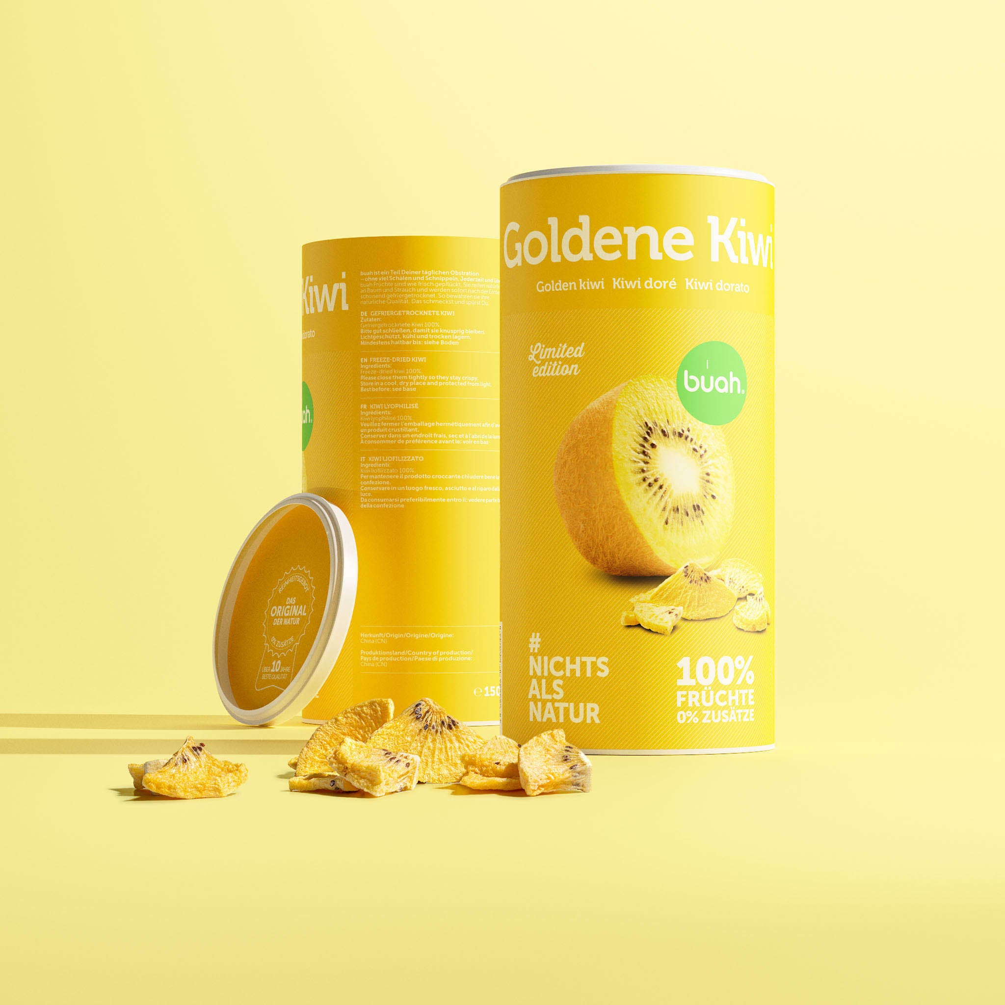Eine gelbe Dose buah gefriergetrocknete Goldene Kiwi zeigt ihre Rückseite mit den Zutaten. Dahinter steht leicht versetzt eine zweite Dose, an die der Deckel lehnt. Davor liegen helle Fruchtstücke auf einem hellgelben Hintergrund.