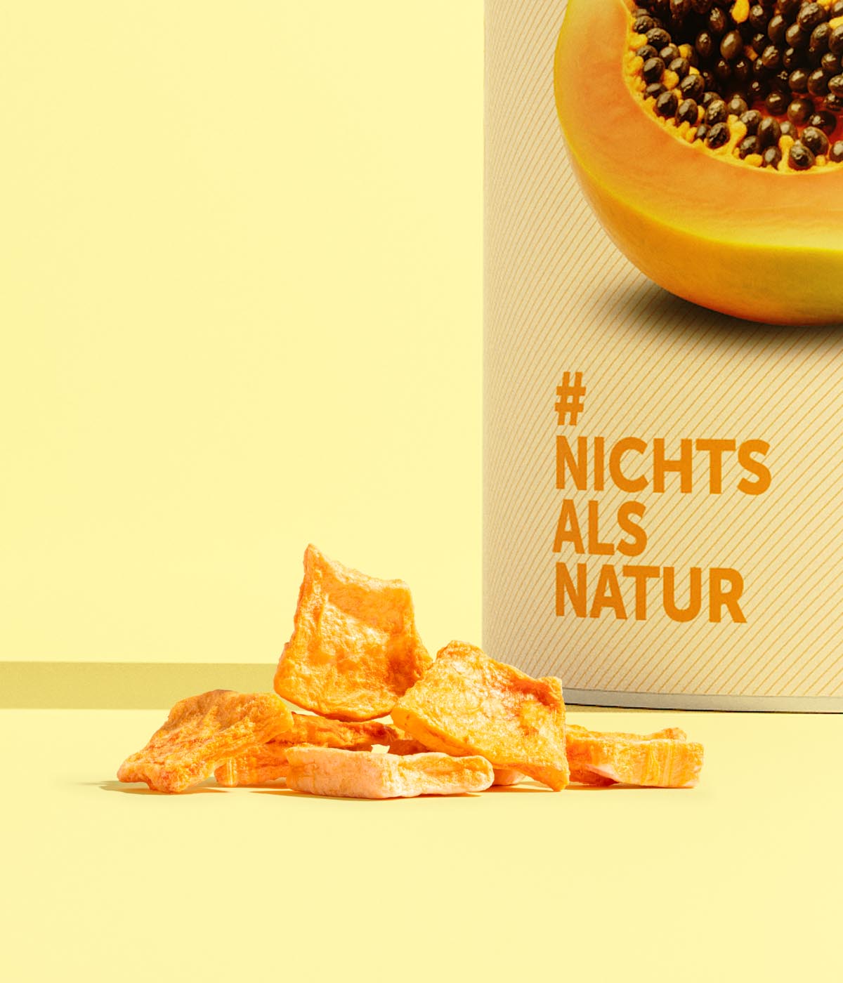 Vertikales Motiv mit einer buah-Dose „Papaya&Limette“ mit gefriergetrockneter Papyastückchen vor der Dose auf gelbem Hintergrund; sichtbar: „NICHTS ALS NATUR“.