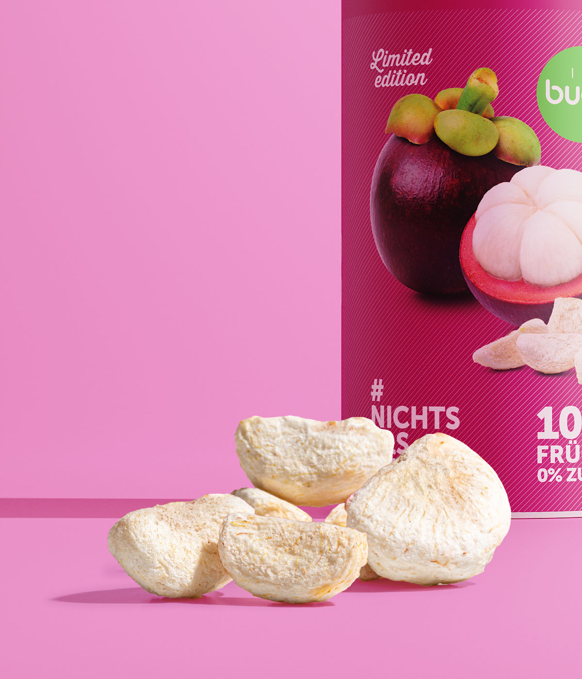 Eine Nahaufnahme von buah gefriergetrockneten Mangostan-Stücken im Vordergrund. Dahinter steht eine angeschnittene Dose der Limited Edition Mangostan vor einem pinken Hintergrund.